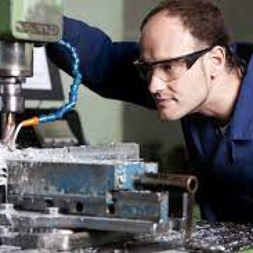 A person using a manual milling machine, wearing safety glasses